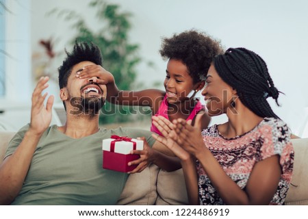 Happy black family at home. African american father, mother and child celebrating birthday, having fun at party.Daughter giving gift to father.