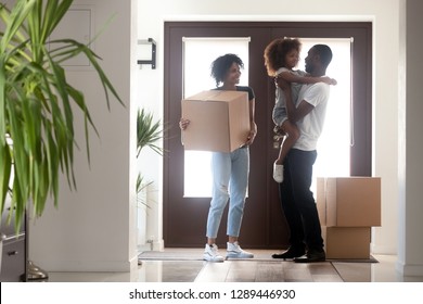 Happy Black Family With Kid Girl Holding Box Entering Into Own House On Moving Day, African American Parents And Child Standing In Hallway, Mortgage, Relocation, Tenants Welcome To New Home Concept