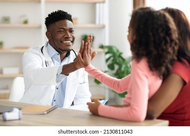 Happy Black Family Mother And Daughter Teenager At Appointment With Male Doctor, Healthy African American Girl Giving Handsome Young Man Pediatrician High Five, Clinic Interior