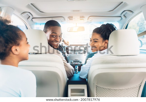 Happy Black Family Of Three Enjoying Car Ride During\
Summer Road Trip On Weekend. Cheerful Parents And Daughter Riding\
New Automobile. Cars Sales And Purchase Concept. Selective Focus,\
Back View