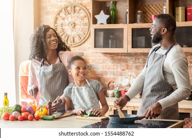 Happy Black Family Of Three Laughing At Kitchen While Making Healthy Dinner, Empty Space