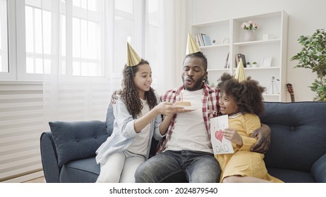 Happy Black Father Blowing Out Birthday Cake Candle, Caring Daughters Congratulating Dad