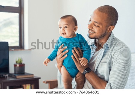 Happy black father and his baby having fun at home. Proud african father holding toddler in arms and playing. Smiling dad loving his cute son.