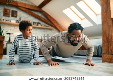 Happy black father and his son doing push-ups while working out together at home.
