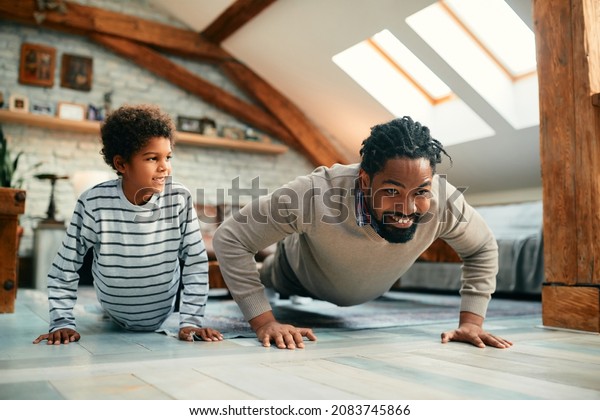 Happy black father and his son doing push-ups\
while working out together at\
home.