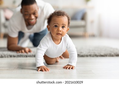 Happy Black Father Looking At Adorable Infant Baby Crawling On Floor At Home, Proud African American Dad Spending Time With His Cute Toddler Child, Enjoying Paternity Leave, Selective Focus