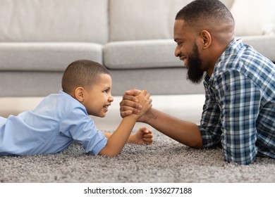 Happy Black Father And Son Armwrestling Lying On Floor Indoors