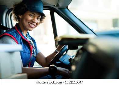 Happy black female courier driving delivery van and looking at camera. 