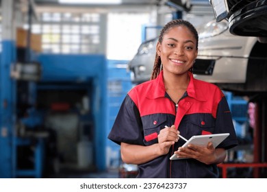 Happy Black female supervisor mechanic, cheerful smile, inspects repair work checklists with tablet at garage, service car maintenance, and fixing specialist occupations in auto transport industry. - Powered by Shutterstock