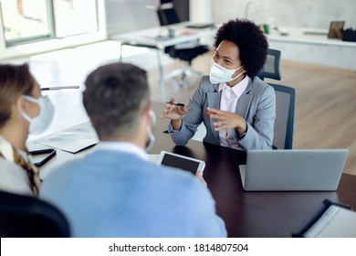 Happy Black Financial Advisor Communicating With A Couple On A Meeting In The Office. All Of Them Are Wearing Protective Face Masks Due To COVID-19 Pandemic. 