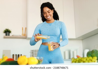 Happy black fit woman having fresh juice for breakfast in the kitchen, pouring beverage from bottle to glass, enjoying healthy eating, free space - Powered by Shutterstock