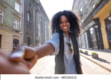 Happy black girl holding a hand and posing for camera. Girl walking aroung the city on a sunny day.