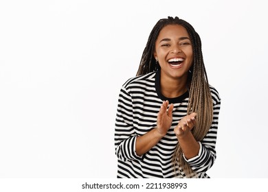 Happy black girl laughing and smiling, applausing, clap hands and looking joyful, standing over white background - Shutterstock ID 2211938993