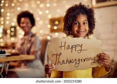 Happy Black Girl With Happy Thanksgiving Sign At Home With Her Mother In The Background. 