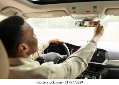 Happy black guy adjusting the rearview mirror while enjoying the car while sitting on the driver's seat