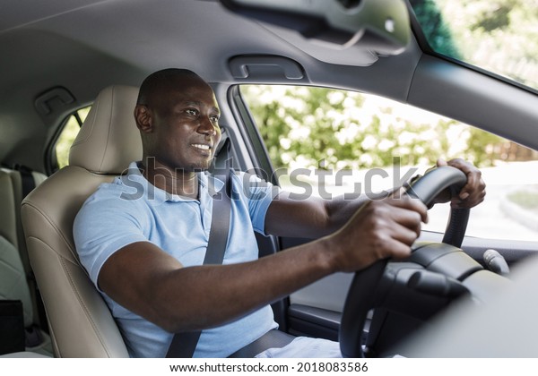 Happy black guy\
in casual driver enjoying driving his new auto, holding hands on\
steering wheel, fasten with seat belt, looking at road and smiling,\
shot from dashboard, copy\
space