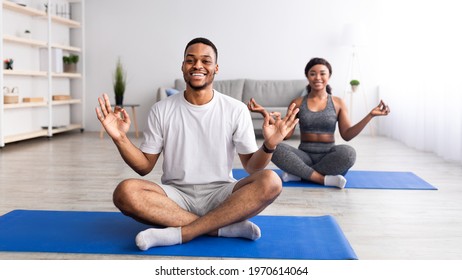 Happy Black Guy Doing Yoga Practice With His Girlfriend, Sitting In Lotus Pose, Making Gyan Mudra At Home, Panorama. Cheerful African American Couple Having Domestic Training During Covid Isolation