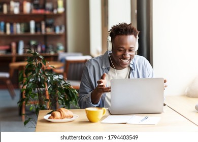 Happy Black Guy In Headphones Communicating Online From Laptop Computer At Coffee Shop, Free Space