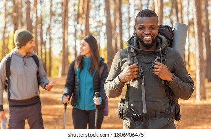 Happy Black Guy Hiking With Caucasian Friends By Countryside, Forest Background