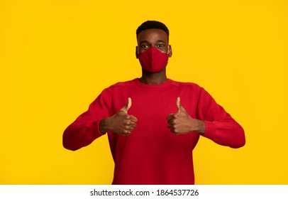 Happy black guy in red protective face mask showing thumbs up at camera, posing isolated on yellow background, african american man support social-distancing during coronavirus pandemic, copy space - Powered by Shutterstock