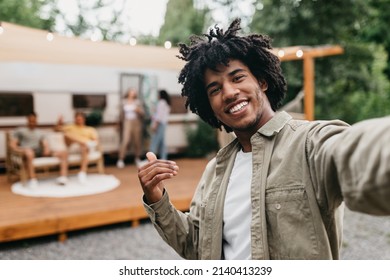 Happy black guy taking selfie near RV, smiling at camera, resting with his multiracial friends outdoors. Cool African American teenager enjoying camping trip, making mobile photo, copy space - Powered by Shutterstock