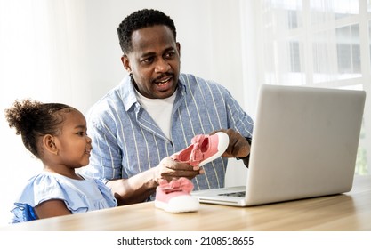 Happy Black Handsome Man With His Little Daughter Using Laptop For Shopping Shoes And Cloth Online At Home. Being A New Baby In Mixed Race Family.