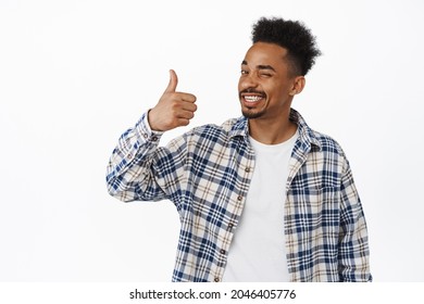Happy Black hipster guy, african american young man shows thumb up in approval, smiling pleased and nod, praise smth good, recommend quality, positive feedback, say yes, white background - Shutterstock ID 2046405776
