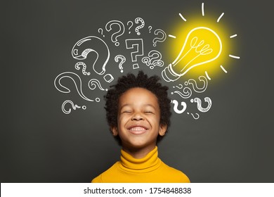 Happy Black Kid On Black Background With Light Bulb And Question Marks. Brainstorming And Idea Concept