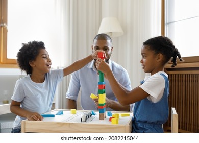 Happy Black Kids Playing Together Building High Plastic Tower On Desk For Board Game, Completing Model From Toy Construction Blocks. Dad Watching Little Sibling Children At Home. Childhood, Daycare