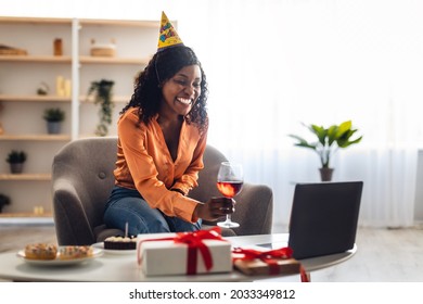 Happy Black Lady Celebrating Birthday Having Remote Online Party Via Video Call On Laptop, Toasting And Clinking Glasses With Computer Webcam At Home. Distance Holiday Celebration