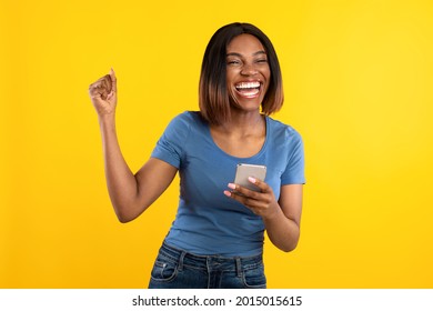 Happy Black Lady Holding Phone Gesturing Yes Winning Mobile Game Over Yellow Background. Studio Shot Of African Woman Celebrating Great News Posing With Cellphone - Shutterstock ID 2015015615