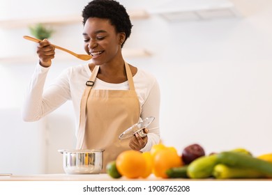 Happy Black Lady Tasting Dinner In Kitchen Cooking Healthy Food Standing Near Table At Home. Nutrition For Weight Loss And Health, Dieting Recipes Concept. Selective Focus