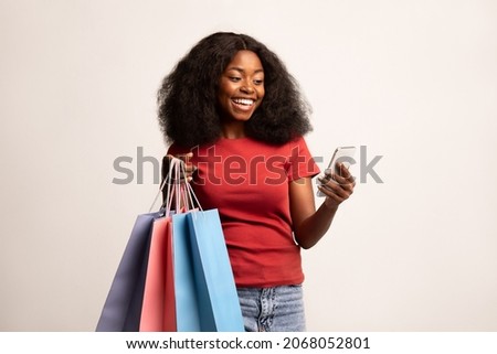Happy Black Lady Using Mobile App On Smartphone For Online Shopping, Cheerful African American Woman Holding Bright Shopper Bags And Cellphone, Enjoying Seasonal Sales And Mobile Offers, Copy Space