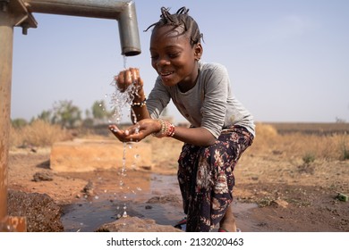 Happy black little girl fooling around with water drops in front of a rough village tap; human right to water and sanitation concept - Shutterstock ID 2132020463