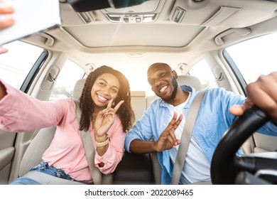 Happy black lovers taking selfie while having car trip, sitting in auto, cheerfully smiling at camera, pretty millennial girlfriend and boyfriend showing v victory peace sign gesture, sun flare - Powered by Shutterstock