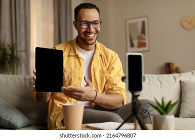 Happy Black Male Blogger Filming Video Review Of New Tablet Computer On Mobile Phone At Home, Mockup. Cheery African American Influencer Promoting Innovative Tech Product, Live Streaming Online