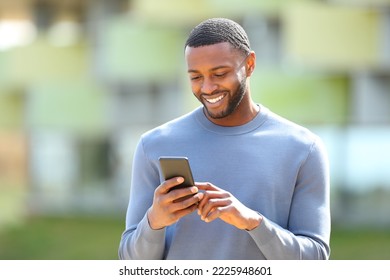 Happy black man checks cell phone walking in the street - Shutterstock ID 2225948601