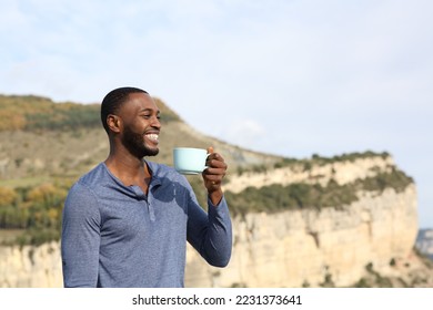 Happy black man drinking coffee contemplating views in the mountain - Powered by Shutterstock