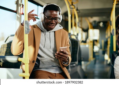 Happy black man having fun while listening music over headphones and using mobile phone in a bus.  - Powered by Shutterstock