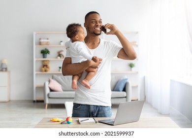 Happy Black Man Holding Baby And Talking On Cellphone While Working At Home Office, Busy African American Father Spending Time With Toddler Child And Managing Business Remotely During Paternity Leave - Powered by Shutterstock