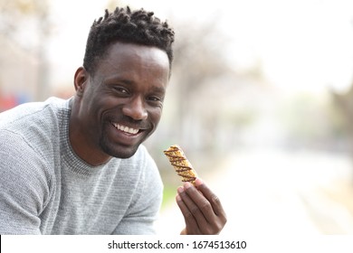 Happy Black Man Holding Granola Bar Ready For Eat Looking At Camera In A Park With Copy Space