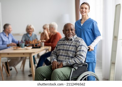 Happy black man older patient on wheelchair with female nurse smiling at camera, group of senior people sitting on couch on background, nursing home interior, healthcare for elderly people concept