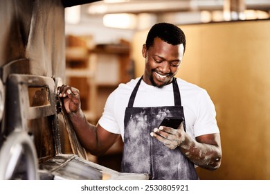 Happy, black man and phone with machinery at bakery for social media, new recipe or browsing ingredients. Young African, male person or baker with smile on mobile smartphone for pastry production - Powered by Shutterstock