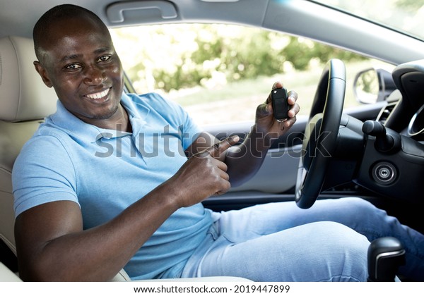 Happy black man pointing at automatic key from his\
new car, side view. Cheerful african american driver renting or\
buying automobile, recommending auto salon or leasing service, copy\
space