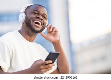 Happy black man smiling listening to music looking at the phone in the street