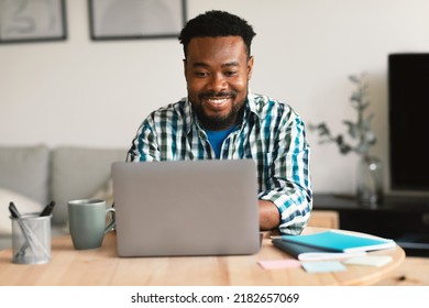 Happy Black Man Using Laptop Computer Browsing Internet Working Online Remotely Sitting At Desk In Modern Office. Distance Job And Web Technology Concept. Front View