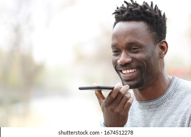 Happy Black Man Using Voice Recognition On Smart Phone Outdoors In A Park