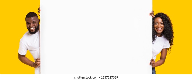 Happy black man and woman standing next to blank placard for advert. Cheerful african american couple in love holding empty board for advertisement or text over yellow studio background, panorama - Shutterstock ID 1837217389