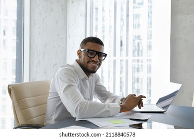 Happy Black Millennial Employee In Glasses, Formalwear Working On Project At Laptop, Analyzing Documents, Paper Reports. Male Professional Head Shot Portrait At Office Workplace