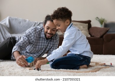 Happy Black Millennial Father And Cute Curly Haired Son Playing Together, Modeling City Road, Driving Toy Car, Relaxing On Warm Heating Carpeted Floor. African Dad And Little Kid Enjoying Game At Home